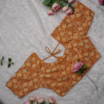 An orange and beige printed blouse piece with a tie neckline, laid flat on a white textured background with pink roses as decorative props.